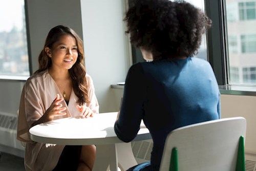 two peers sitting across a small cafe table from one another in the afternoon training